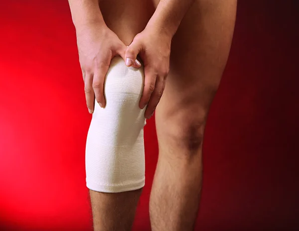 Joven con vendaje elástico en la rodilla, sobre fondo rojo — Foto de Stock