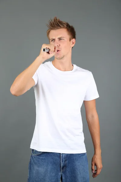 Schöner junger Mann singt auf grauem Hintergrund — Stockfoto