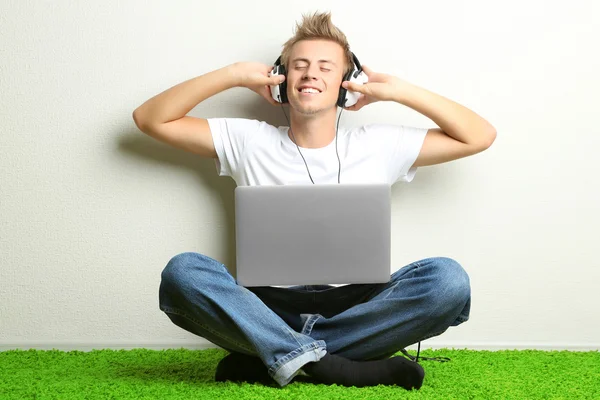 Ung man koppla på mattan och lyssna på musik, på grå vägg bakgrund — Stockfoto