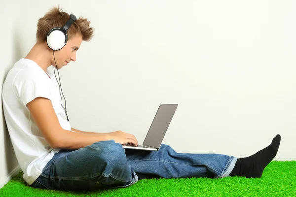 Hombre joven relajándose en la alfombra y escuchando música, sobre fondo gris de la pared — Foto de Stock