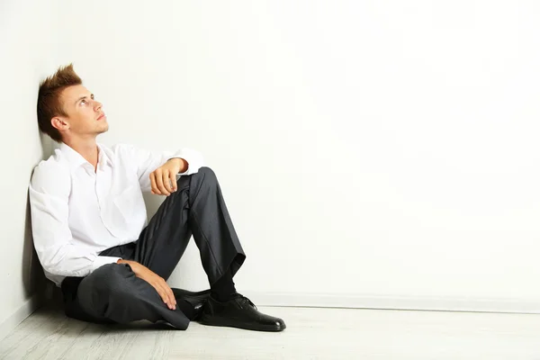 Young businessman sitting on floor, on gray wall background — Stock Photo, Image