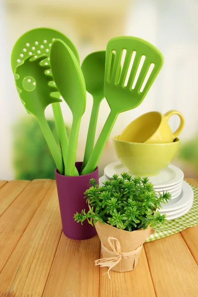 Ustensiles de cuisine en plastique dans le stand avec vaisselle propre sur la table sur fond lumineux — Photo