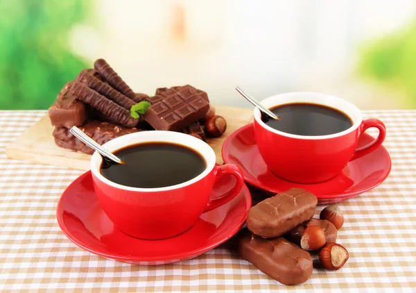 Tazas rojas de café fuerte con barras de chocolate en mantel sobre fondo brillante —  Fotos de Stock