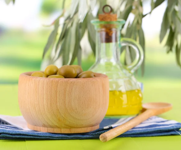 Olivolja och Oliver i skål på servett på träbord på natur bakgrund — Stockfoto