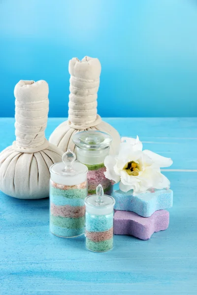 Aromatic salts in glass bottles and herbal compress balls for spa treatment, on blue background — Stock Photo, Image