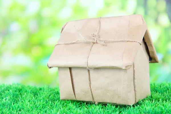Casa envuelta en papel kraft marrón, sobre hierba verde, sobre fondo natural —  Fotos de Stock