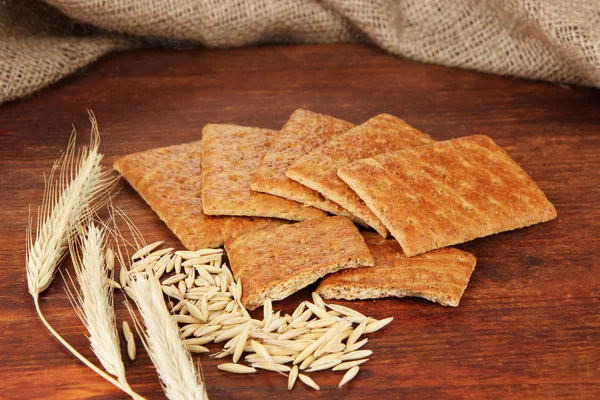 Delicious crackers with spikes and corn on wooden table on sackcloth background — Stock Photo, Image