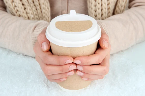 Hot drink in paper cup in hands with snow close up — Stock Photo, Image