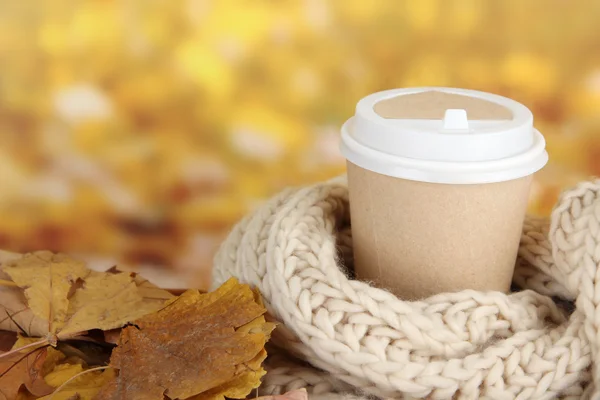 Warme drank in papier cup met sjaal en gele bladeren op lichte achtergrond — Stockfoto