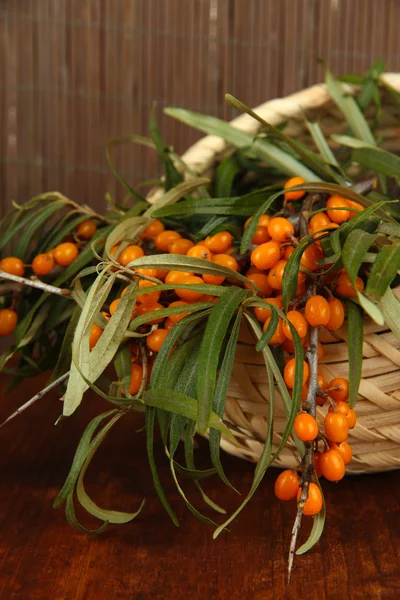 Branches of sea buckthorn in basket on table on bamboo background — Stock Photo, Image