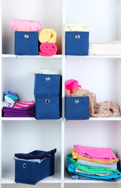 Blue textile boxes with towels and clothes in white shelves — Stock Photo, Image