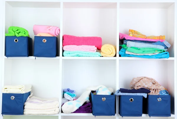 Blauwe textiel vakken met handdoeken en kleren in witte planken — Stockfoto