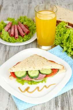 Lezzetli sandviç salam sosis ve ahşap masa arka plan üzerinde renkli peçete üzerinde sebze ve meyve suyu ile kompozisyon