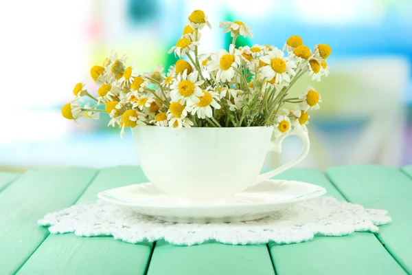 Bouquet of chamomile flowers in cup, on bright background — Stock Photo, Image