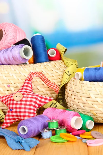 Wicker baskets with accessories for needlework on wooden table, on bright background — Stock Photo, Image