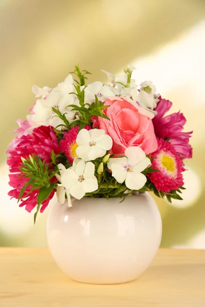 Beautiful bouquet of bright flowers in color vase, on wooden table, on bright background — Stock Photo, Image