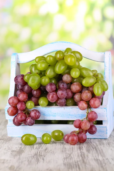 Uvas verdes e roxas maduras em cesta sobre mesa de madeira sobre fundo natural — Fotografia de Stock
