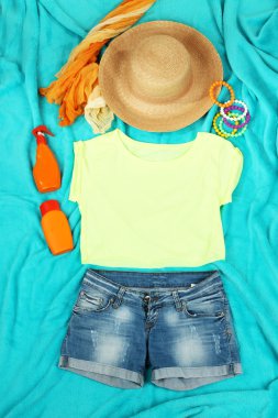 Top, shorts and beach items on bright blue background