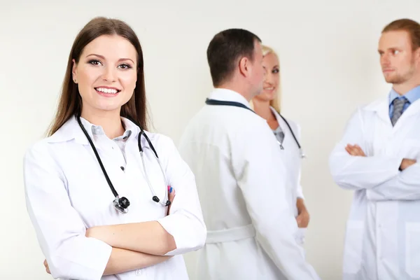 Médico em pé na frente de colegas de trabalho em fundo cinza — Fotografia de Stock