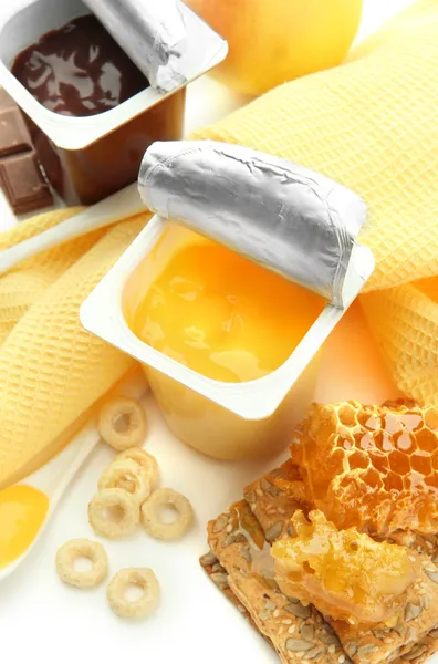 Dolci saporiti in bicchieri di plastica aperti e favi di miele, frutta e fiocchi su tovagliolo, isolati su bianco — Foto Stock