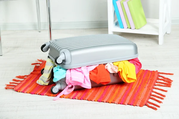 Koffer mit Kleidung auf Matte auf Zimmerhintergrund — Stockfoto