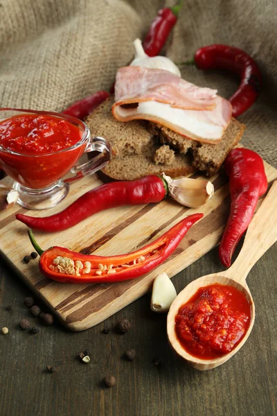 Komposisi dengan saus salsa pada roti, cabai merah panas dan bawang putih, pada kain karung, di latar belakang kayu — Stok Foto