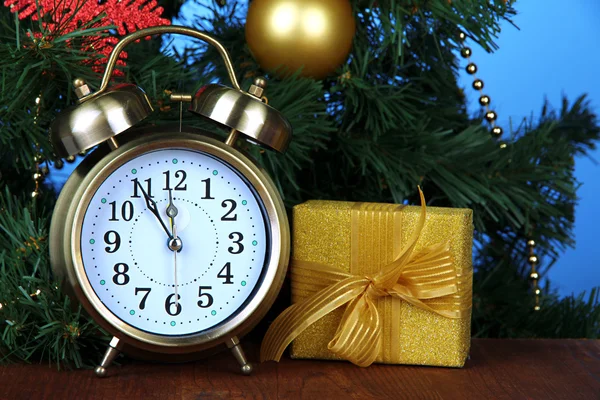 Alarm clock with Christmas tree and present on table on blue background — Stock Photo, Image