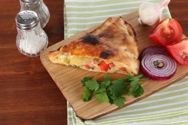 Pizza calzone on wooden board on napkin on wooden table — Stock Photo, Image