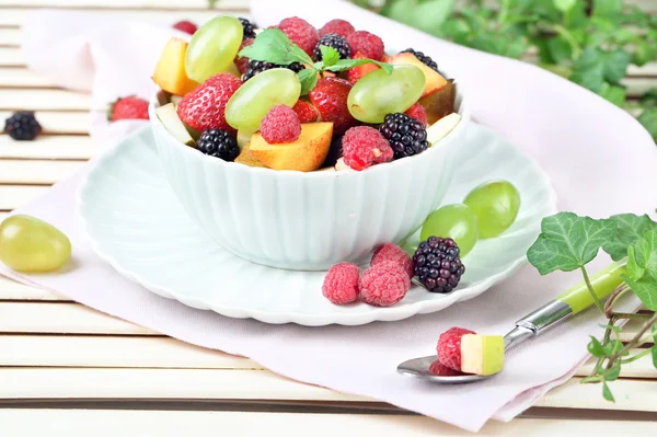 Salada de frutas na tigela, na mesa de madeira, no fundo brilhante — Fotografia de Stock