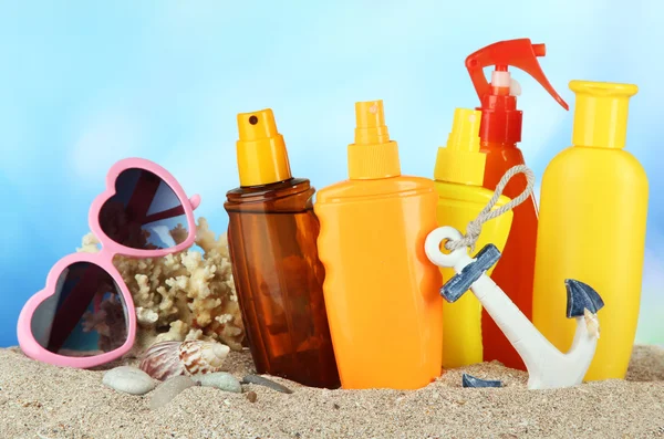 Botellas con crema bronceadora y gafas de sol, sobre fondo azul — Foto de Stock