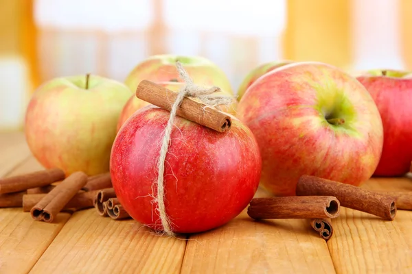 Ripe apples with with cinnamon sticks on wooden table, on bright background — Stock Photo, Image