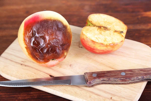 Гнилые яблоки на деревянной доске на столе — стоковое фото