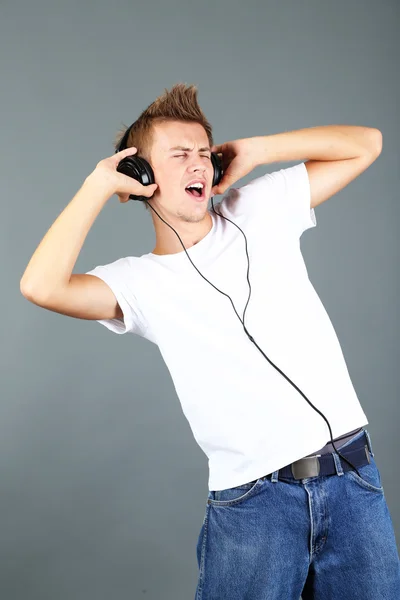 Przystojny młodzieniec, słuchanie muzyki na szarym tle — Zdjęcie stockowe
