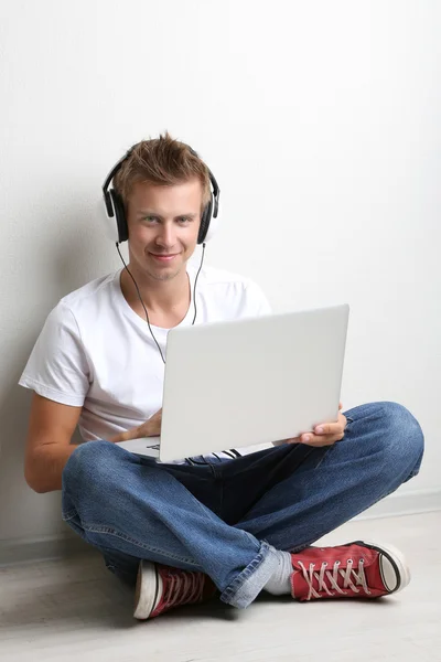 Schöner junger Mann hört Musik auf grauem Hintergrund — Stockfoto