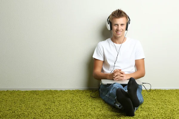 Jonge man ontspannen op tapijt en luisteren naar muziek, op grijze muur achtergrond — Stockfoto