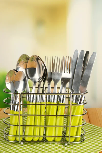 Facas, garfos e colheres em suporte de metal na mesa sobre fundo brilhante — Fotografia de Stock