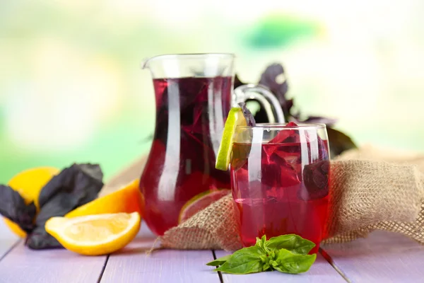 Red basil lemonade in jug and glass, on wooden table, on bright background — Stock Photo, Image