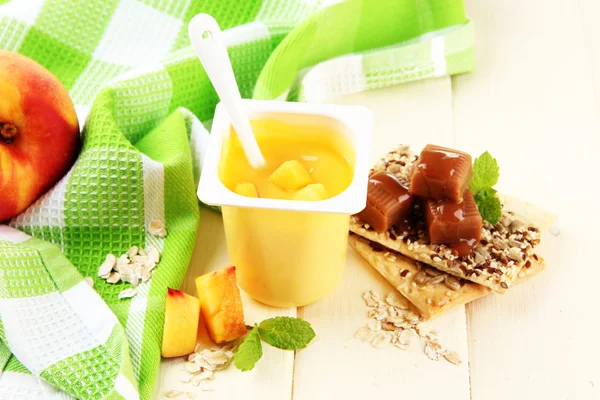 Läckra yoghurt med bitar av färsk frukt, kakor och flingor, på färg trä bakgrund — Stock fotografie