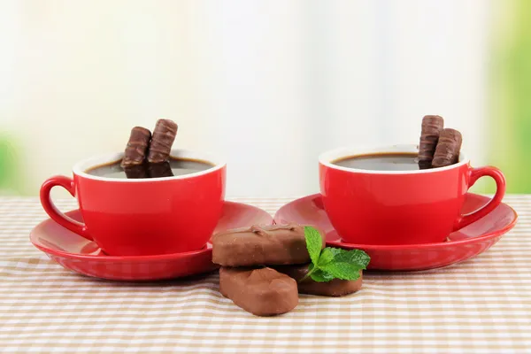 Copos vermelhos de café forte e barras de chocolate na toalha de mesa em fundo brilhante — Fotografia de Stock