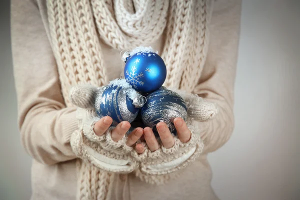 Weibliche Hände in Fäustlingen Weihnachtsbaumkugeln, auf farbigem Hintergrund — Stockfoto