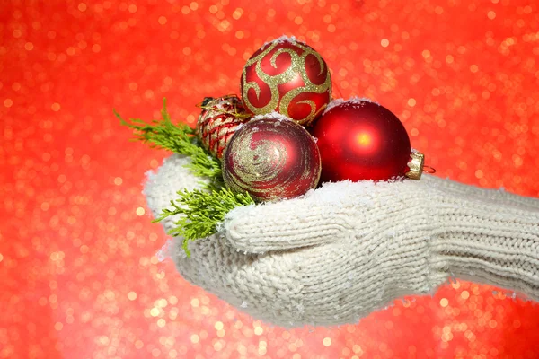 Vrouwelijke handen in wanten kerstboom ballen, op een achtergrond met kleur — Stockfoto