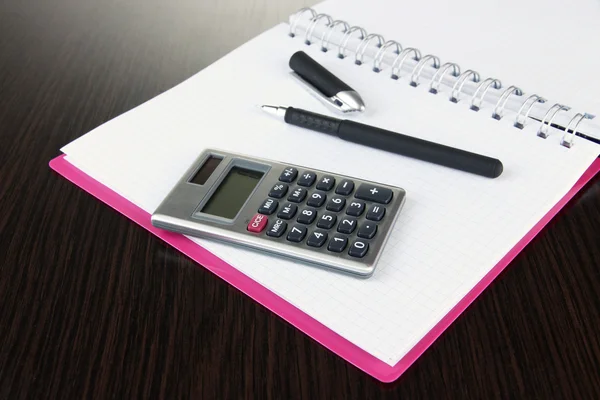 Caderno com caneta e calculadora sobre fundo de madeira — Fotografia de Stock