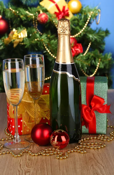 Bottle of champagne with glasses and Christmas balls on wooden table on Christmas tree background — Stock Photo, Image