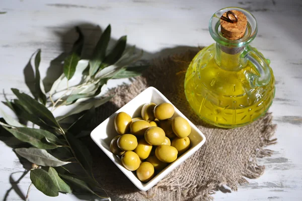 Olive oil and olives in bowl on sackcloth on wooden table — Stock Photo, Image