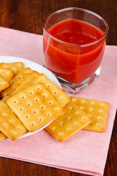 Вкусные крекеры с томатным соком и салфеткой на деревянном фоне — стоковое фото