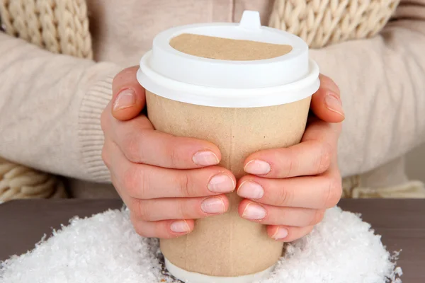 Hot drink in paper cup in hands with snow on wooden table close up — Stock Photo, Image