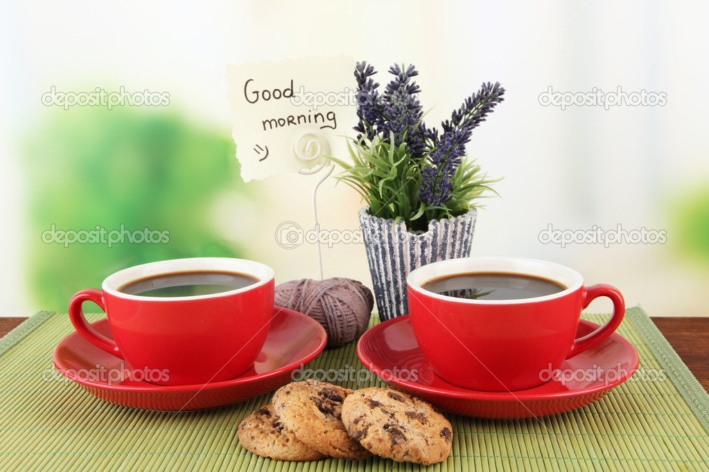 Red cups of strong coffee with cookies and flowers on bamboo mat on bright background