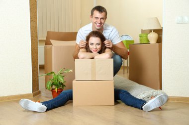 Young couple with boxes in new home on room background clipart