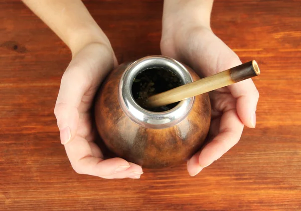 Woman hands holding calabash and bombilla with yerba mate on wooden background — Stock Photo, Image