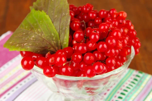 Червоні ягоди калини у скляній вазі на серветці на дерев'яному фоні — стокове фото